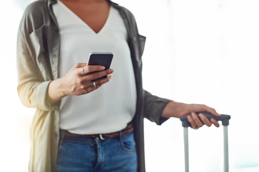 Traveler holding a phone and suitcase handle while setting up her device