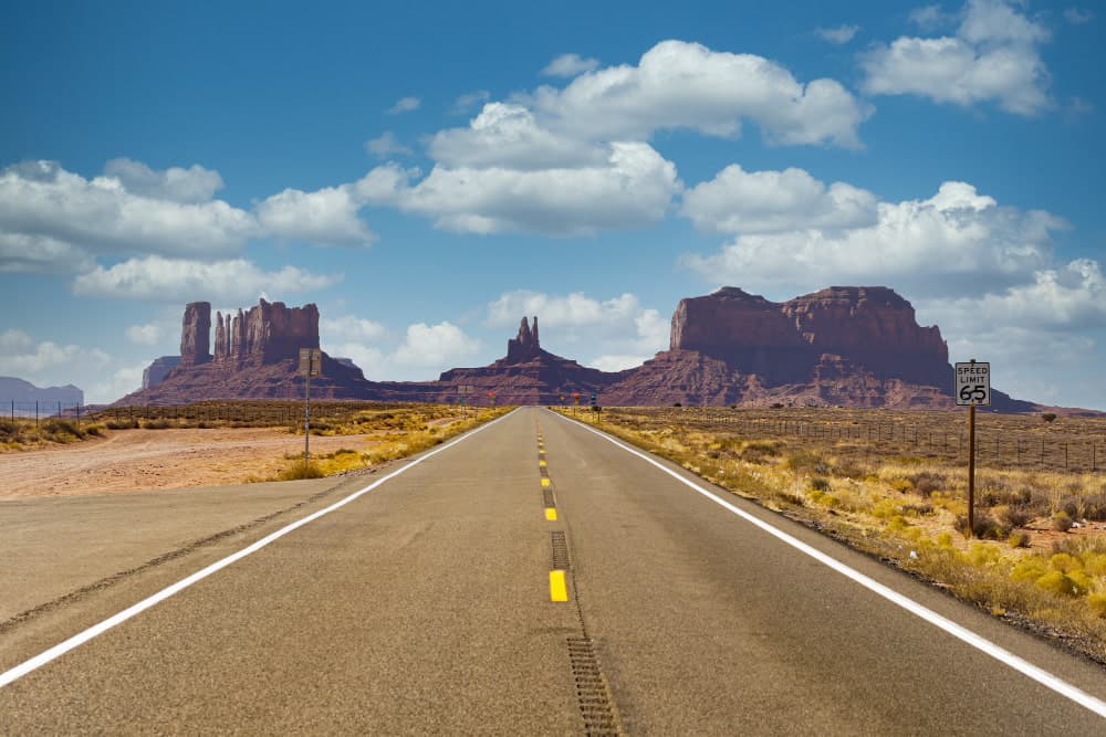 Open highway leading to Monument Valley with red rock formations under a blue sky.