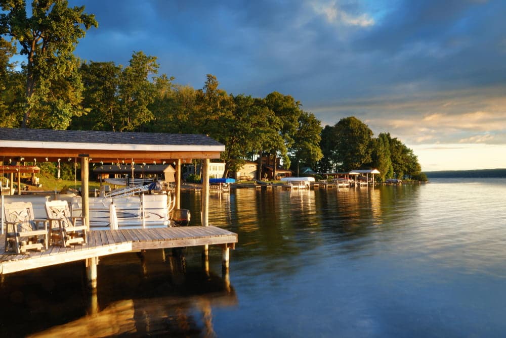 Lakeside dock with boats and chairs at sunset, surrounded by trees and calm water.