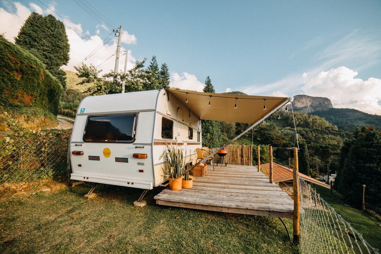 Vintage camper trailer with awning and wooden deck in a scenic mountain setting.