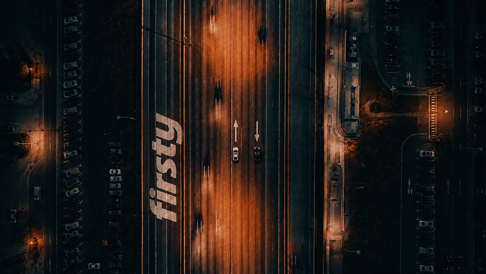 Aerial view of a multi-lane highway at dusk with two cars driving in opposite directions, the Firsty logo painted on the road, illustrating automatic network switching between mobile carriers for always-on global connectivity.
