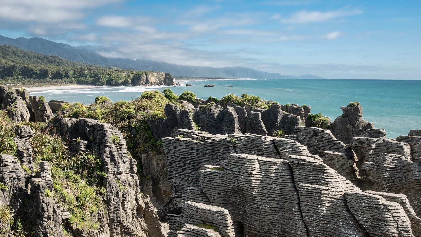 Pancake-rock limestone formations at a coastal lookout, their layered columns rising above turquoise sea under a clear sky.