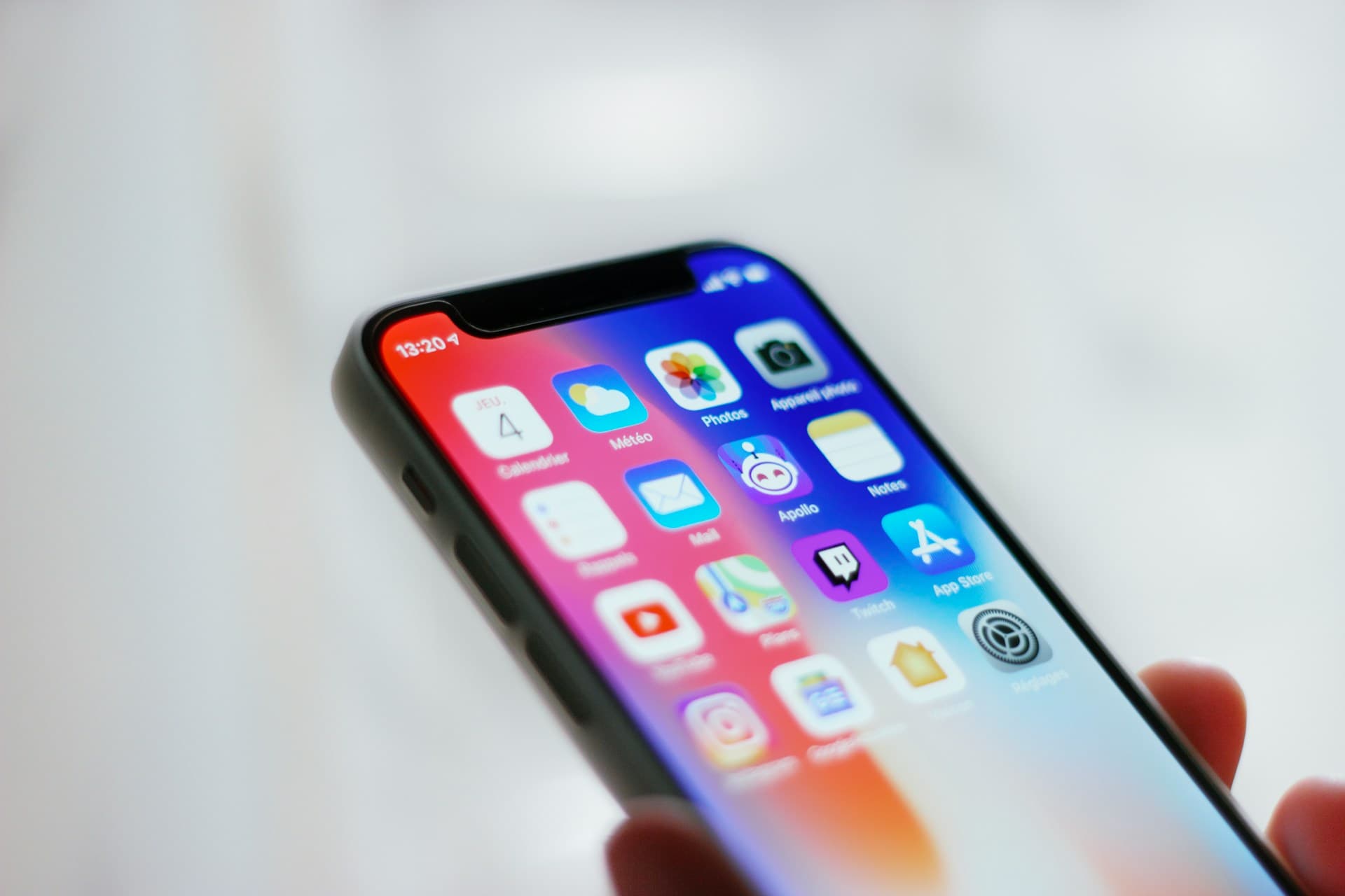 Hand holding smartphone displaying colorful home-screen app icons against a blurred white background.