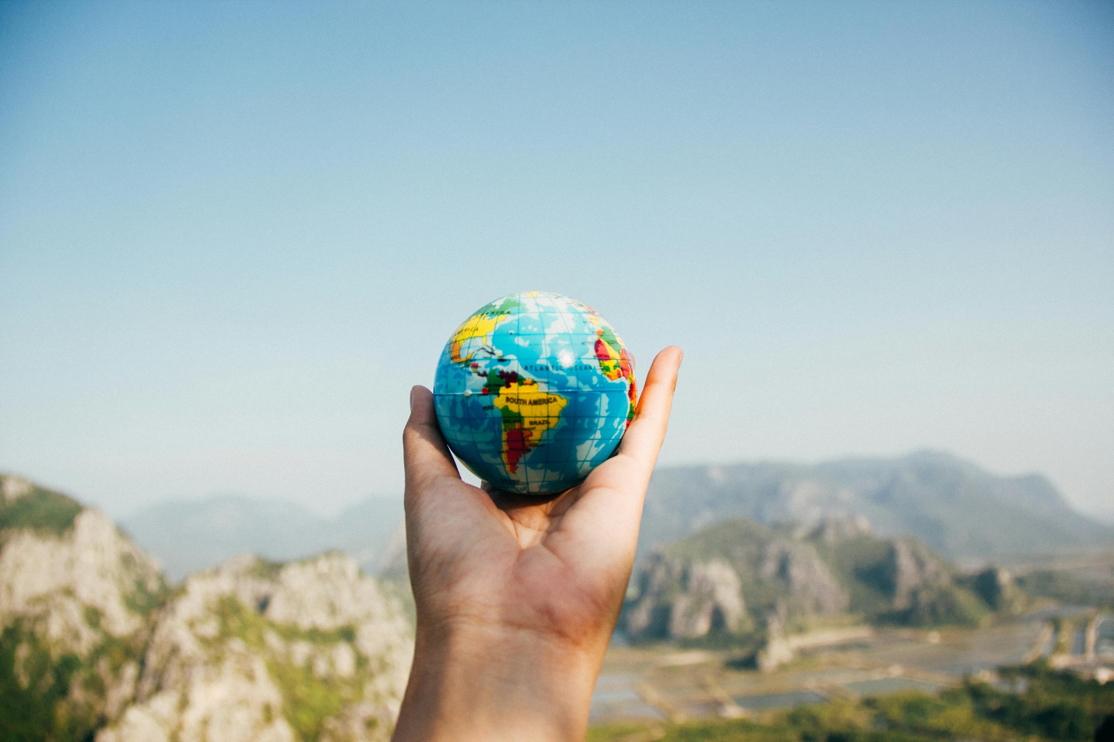 Hand holding a small globe against a mountain backdrop