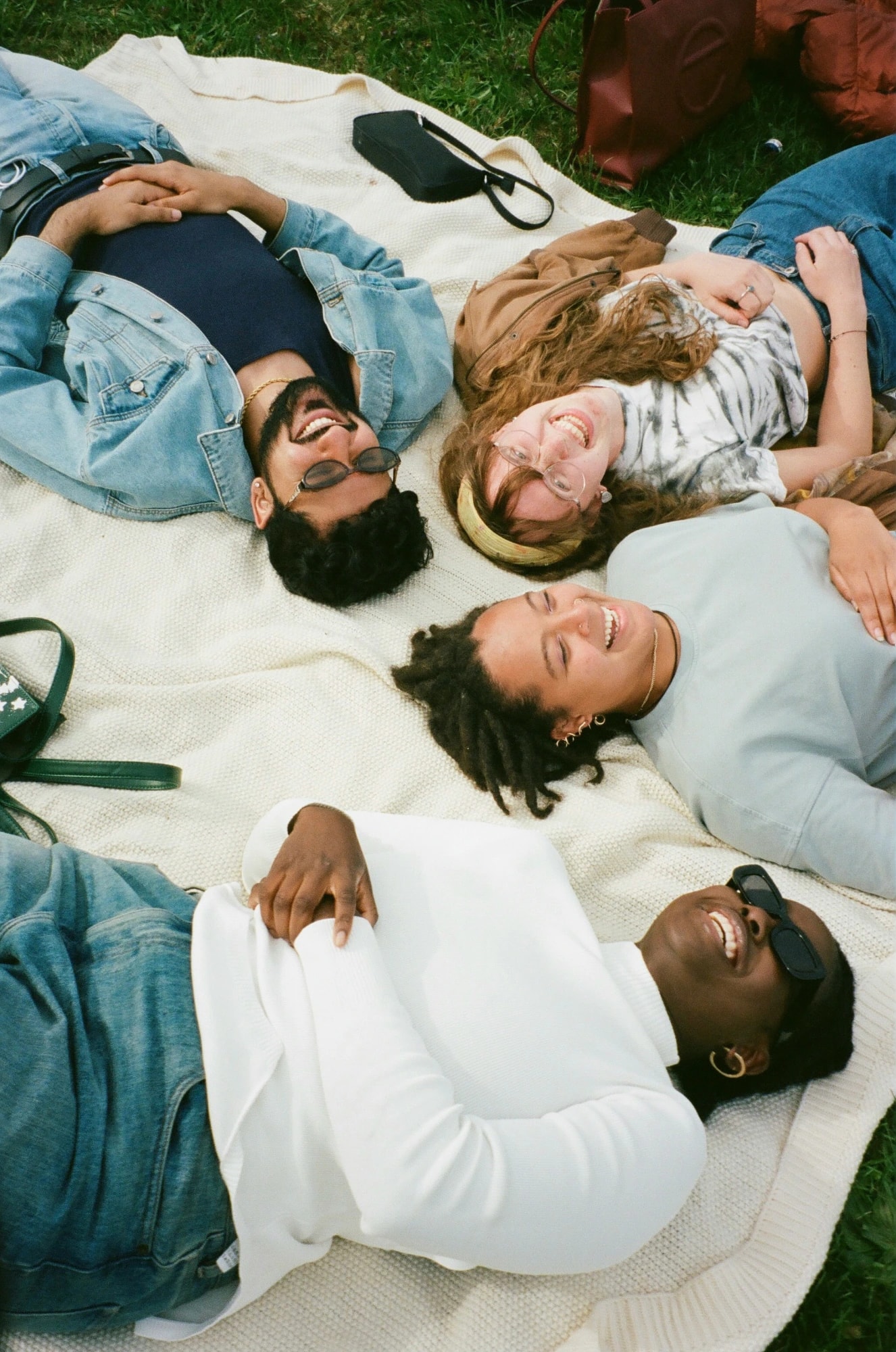 Five friends lying on a blanket on the grass, laughing