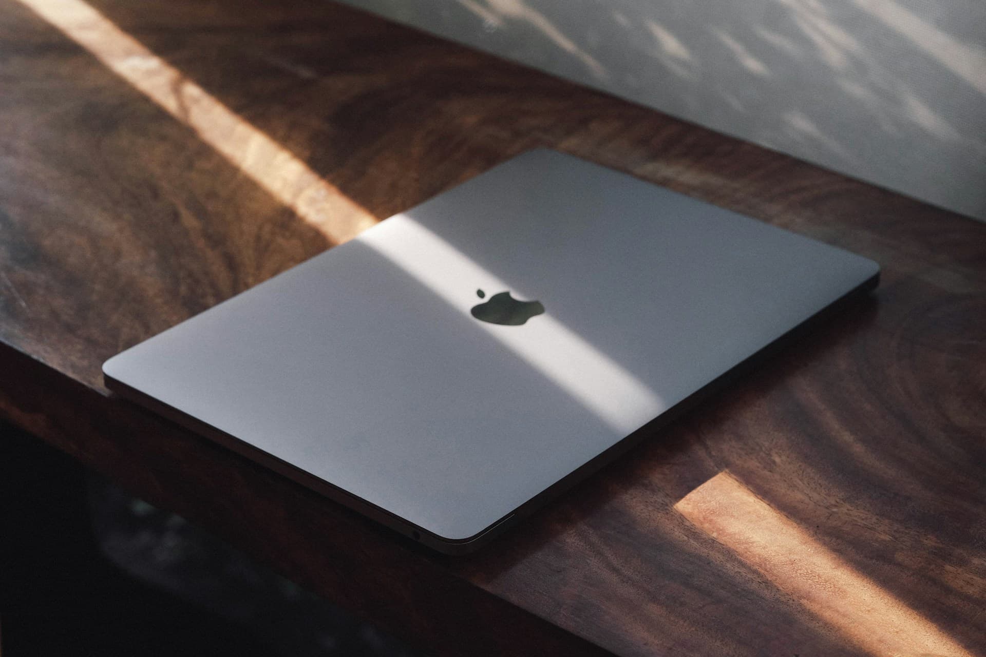 Closed MacBook on a wooden desk in sunlight